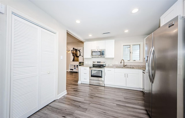 kitchen featuring white cabinets, sink, light stone countertops, appliances with stainless steel finishes, and light hardwood / wood-style floors