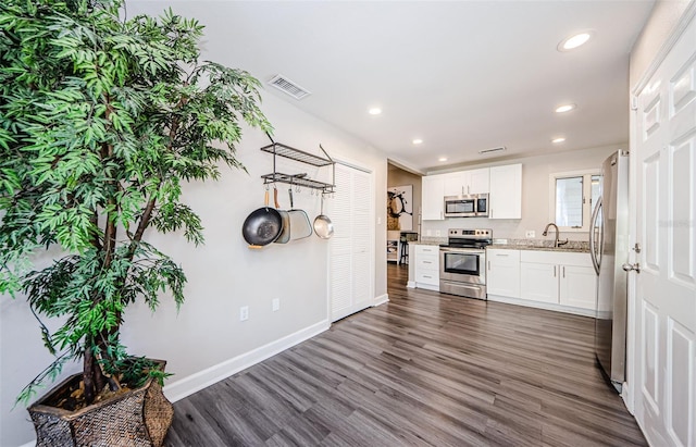 kitchen featuring dark hardwood / wood-style flooring, light stone counters, stainless steel appliances, sink, and white cabinets