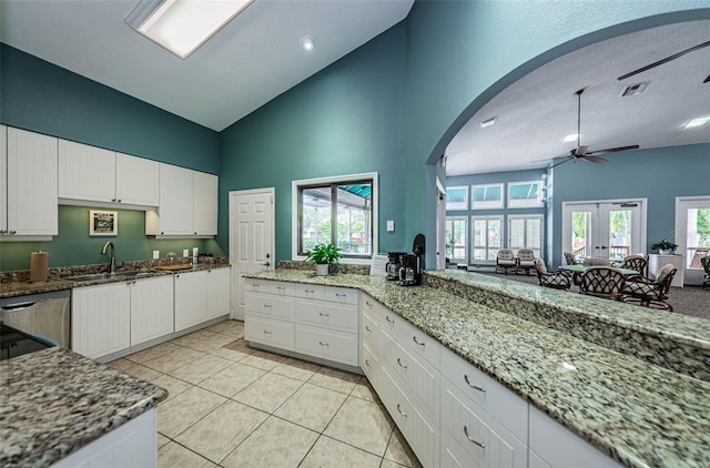 kitchen featuring light stone countertops, french doors, white cabinets, and high vaulted ceiling