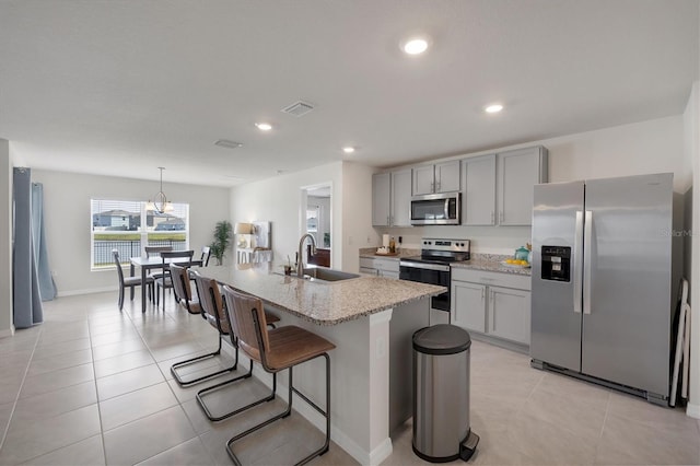 kitchen featuring sink, light stone counters, a kitchen island with sink, gray cabinetry, and appliances with stainless steel finishes