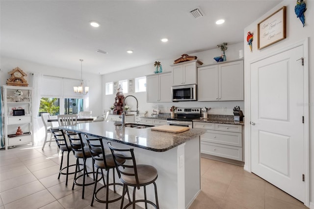 kitchen with decorative light fixtures, stainless steel appliances, a center island with sink, white cabinetry, and sink