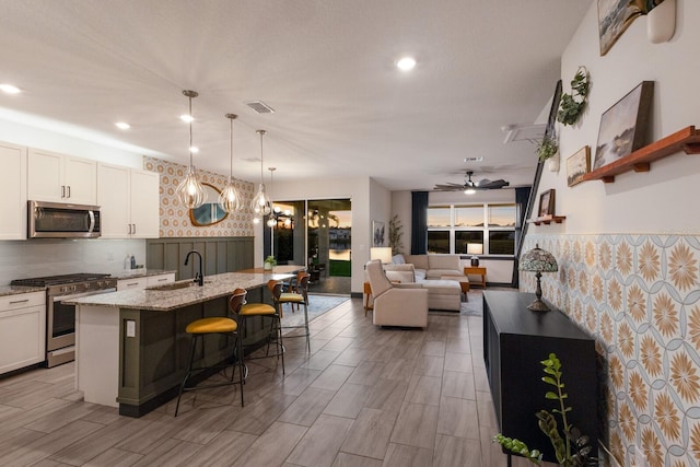 kitchen featuring appliances with stainless steel finishes, white cabinets, light stone countertops, a breakfast bar, and an island with sink