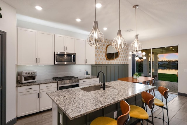 kitchen featuring sink, white cabinets, a kitchen island with sink, and appliances with stainless steel finishes