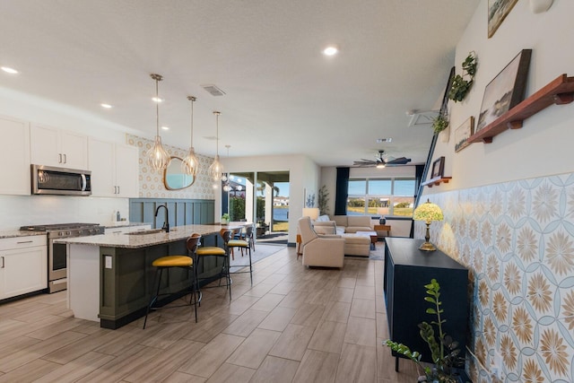 kitchen featuring a kitchen breakfast bar, hanging light fixtures, white cabinets, a center island with sink, and stainless steel appliances