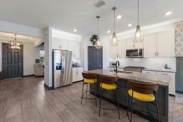 kitchen featuring appliances with stainless steel finishes, white cabinetry, dark stone counters, an island with sink, and sink