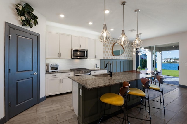 kitchen featuring sink, white cabinetry, appliances with stainless steel finishes, and an island with sink