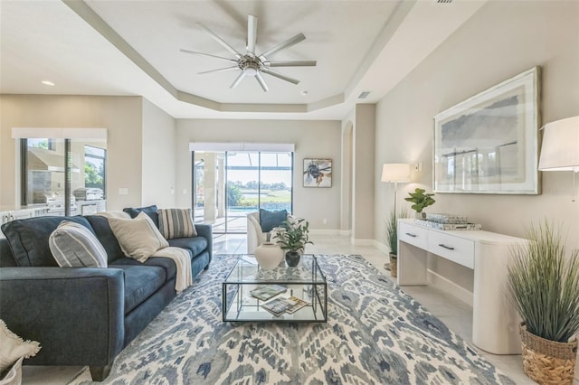 tiled living room featuring ceiling fan and a tray ceiling