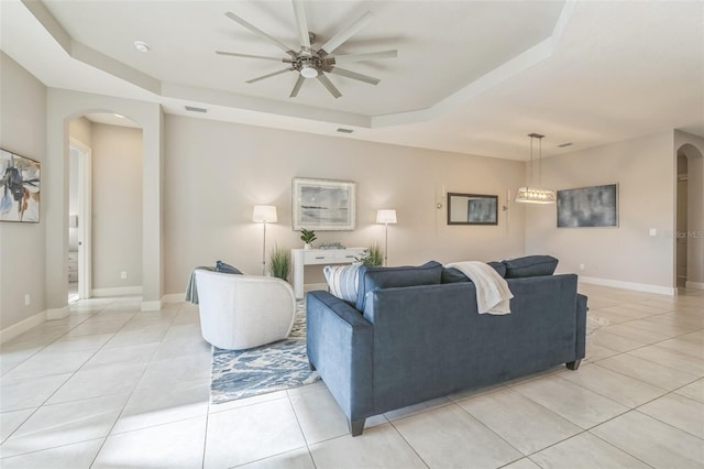 tiled living room featuring a raised ceiling and ceiling fan with notable chandelier