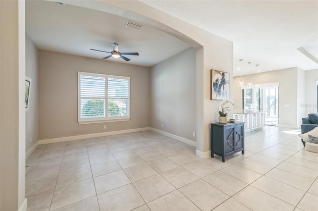 tiled spare room featuring ceiling fan with notable chandelier