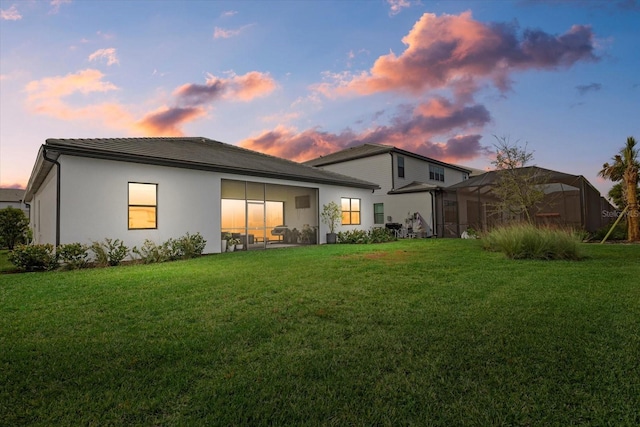 back house at dusk featuring a lanai and a yard