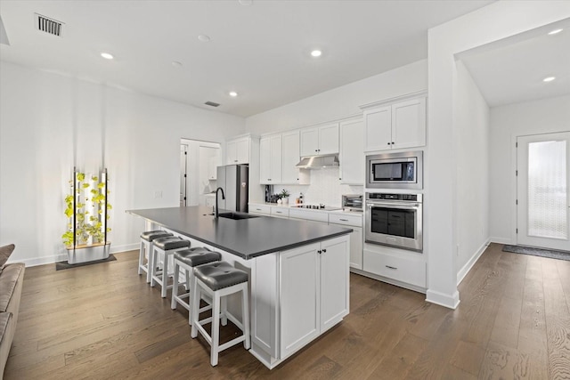 kitchen with white cabinets, appliances with stainless steel finishes, a kitchen bar, sink, and a center island with sink