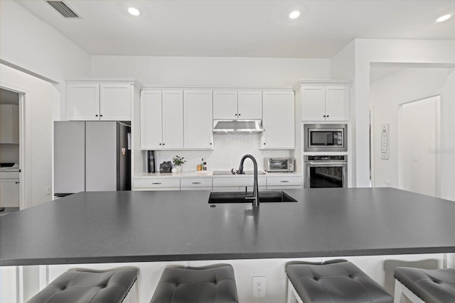 kitchen with white cabinets, appliances with stainless steel finishes, sink, and a center island with sink