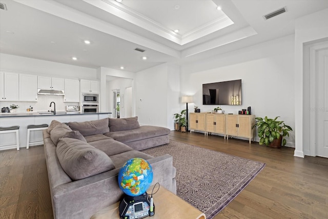 living room featuring a raised ceiling, dark hardwood / wood-style floors, sink, and crown molding