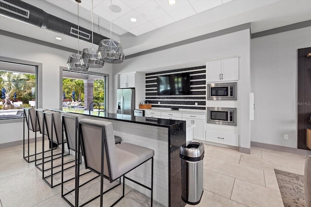 kitchen featuring white cabinetry, appliances with stainless steel finishes, a kitchen breakfast bar, hanging light fixtures, and sink