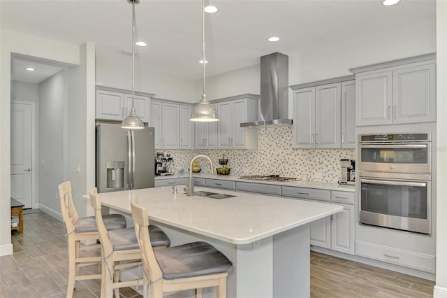 kitchen with sink, a center island with sink, appliances with stainless steel finishes, and wall chimney exhaust hood