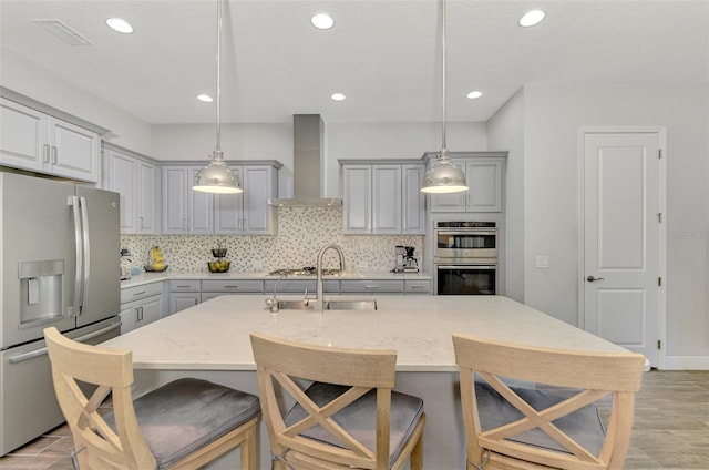 kitchen featuring stainless steel appliances, sink, decorative light fixtures, backsplash, and wall chimney range hood