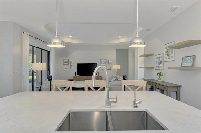 kitchen with decorative light fixtures, a tray ceiling, light stone counters, and sink