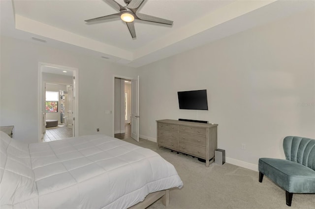 bedroom with ensuite bath, light colored carpet, ceiling fan, and a tray ceiling