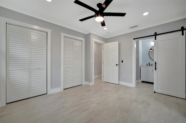 unfurnished bedroom with ceiling fan, light wood-type flooring, connected bathroom, and a barn door