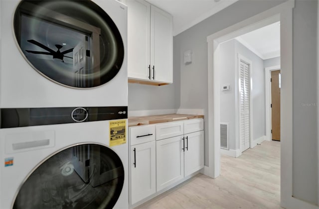 clothes washing area featuring ornamental molding, cabinets, light wood-type flooring, and stacked washer and dryer