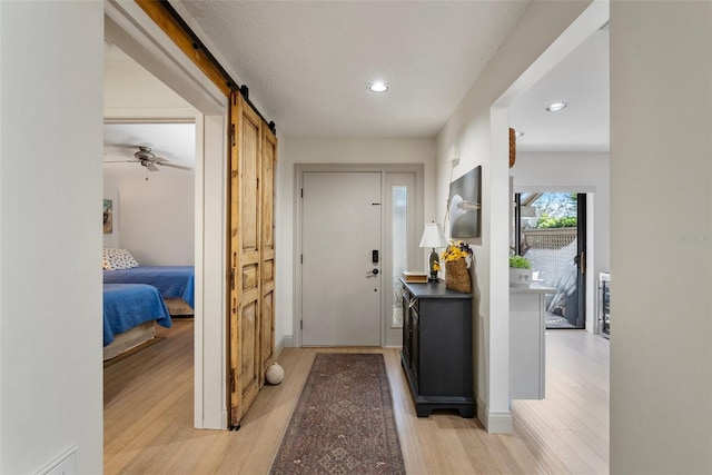 foyer with ceiling fan, a barn door, and light wood-type flooring