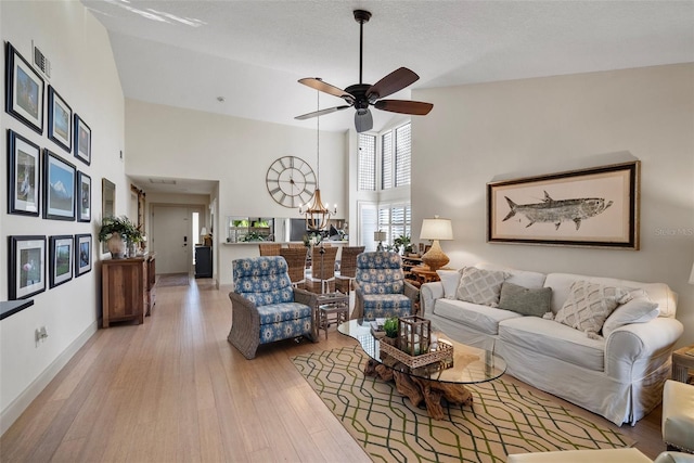 living room with ceiling fan with notable chandelier, high vaulted ceiling, and light wood-type flooring