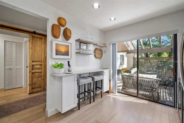 interior space with white cabinetry, a barn door, a breakfast bar, and light wood-type flooring