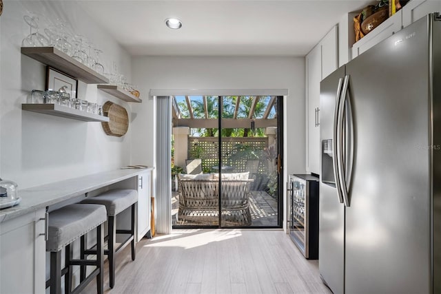 kitchen with wine cooler, a breakfast bar, white cabinetry, stainless steel fridge, and light hardwood / wood-style floors