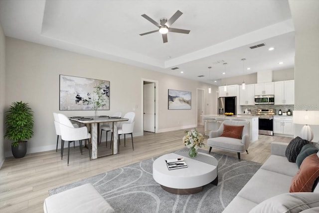 living room featuring light wood-type flooring, a raised ceiling, and ceiling fan