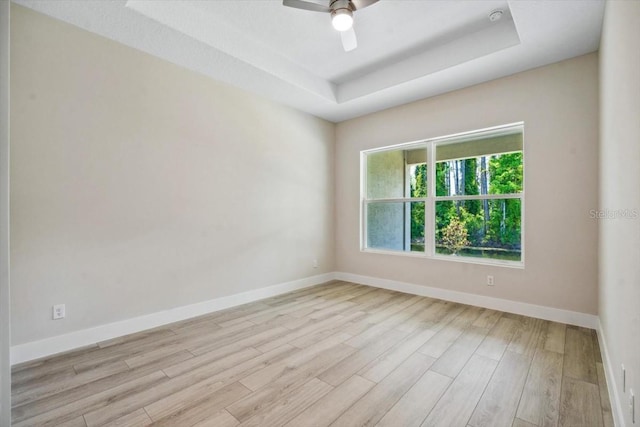 spare room with ceiling fan, light hardwood / wood-style floors, and a tray ceiling