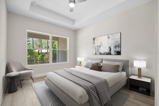 bedroom with a tray ceiling, ceiling fan, and light hardwood / wood-style flooring