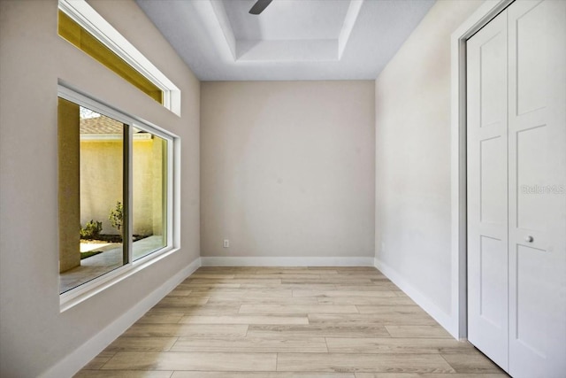 unfurnished room featuring ceiling fan, light hardwood / wood-style floors, a raised ceiling, and a wealth of natural light