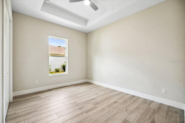 spare room featuring a raised ceiling, ceiling fan, and light hardwood / wood-style flooring