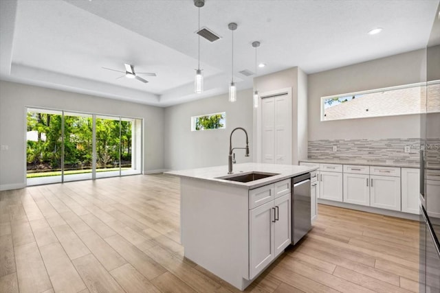 kitchen with white cabinetry, sink, ceiling fan, hanging light fixtures, and an island with sink