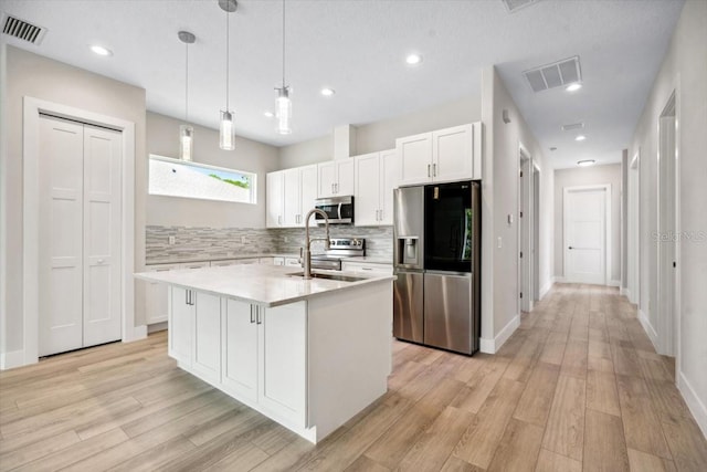 kitchen featuring white cabinetry, an island with sink, decorative light fixtures, decorative backsplash, and appliances with stainless steel finishes