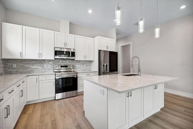 kitchen with appliances with stainless steel finishes, sink, a center island with sink, decorative light fixtures, and white cabinetry