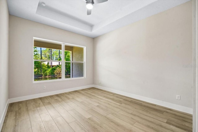 spare room featuring a tray ceiling, ceiling fan, and light wood-type flooring