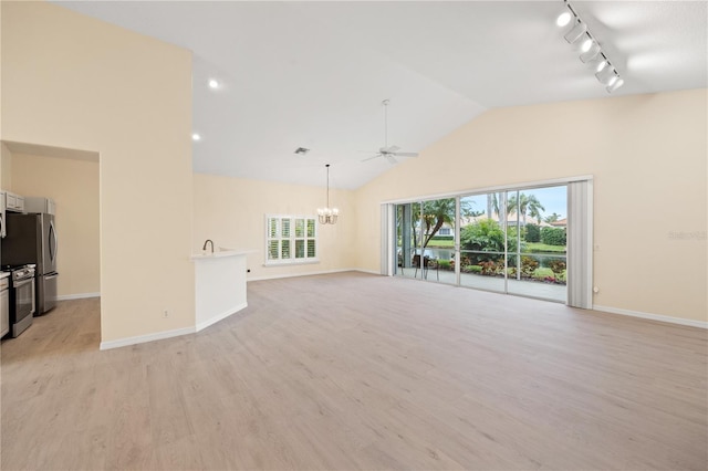 unfurnished living room with a wealth of natural light, ceiling fan with notable chandelier, light wood-style floors, and vaulted ceiling