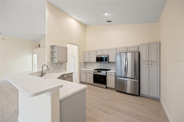 kitchen featuring open shelves, a peninsula, gray cabinets, a sink, and appliances with stainless steel finishes