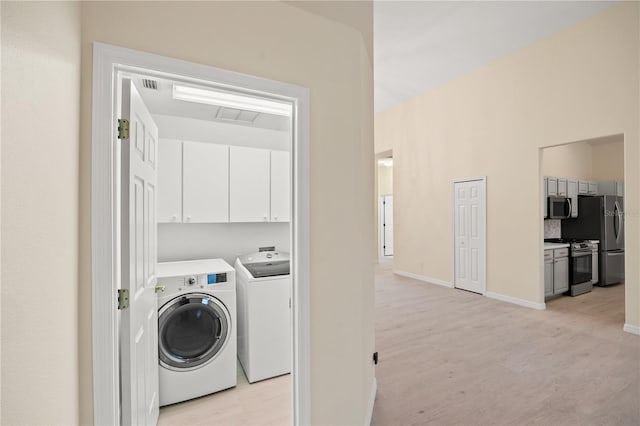 laundry area featuring washing machine and clothes dryer, visible vents, baseboards, light wood-style flooring, and cabinet space