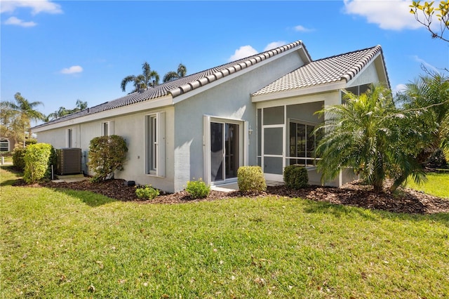 back of house with a tiled roof, stucco siding, a lawn, and a sunroom