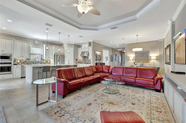 tiled living room with ornamental molding, a raised ceiling, and ceiling fan