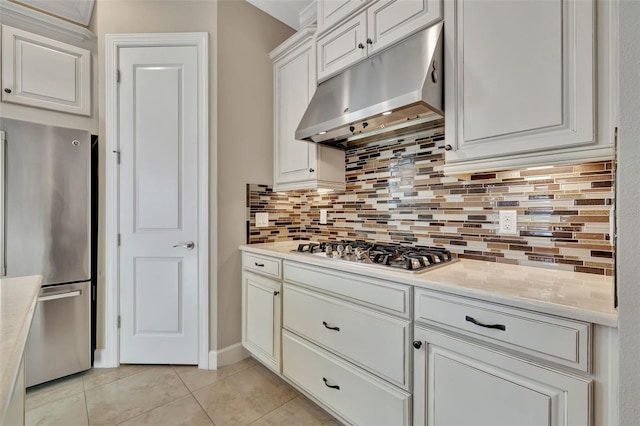 kitchen featuring light stone counters, light tile patterned floors, appliances with stainless steel finishes, white cabinets, and backsplash