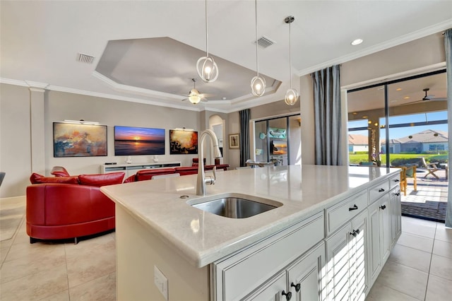 kitchen featuring sink, white cabinets, a raised ceiling, light stone countertops, and a center island with sink