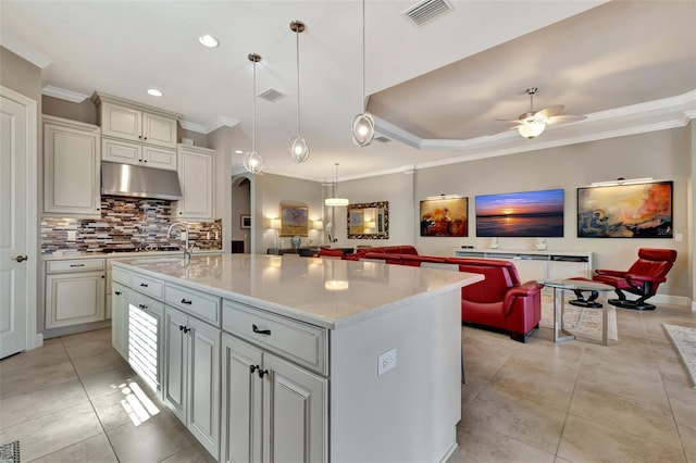 kitchen with pendant lighting, ornamental molding, a center island with sink, and backsplash