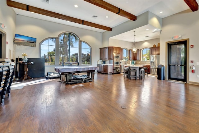 rec room with a towering ceiling, beam ceiling, and dark hardwood / wood-style flooring