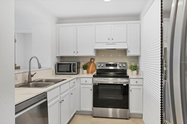 kitchen with appliances with stainless steel finishes, light tile patterned floors, sink, white cabinetry, and backsplash