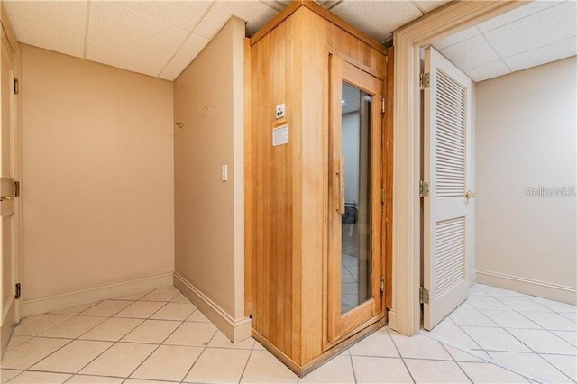 hallway featuring light tile patterned floors, wooden walls, and a drop ceiling