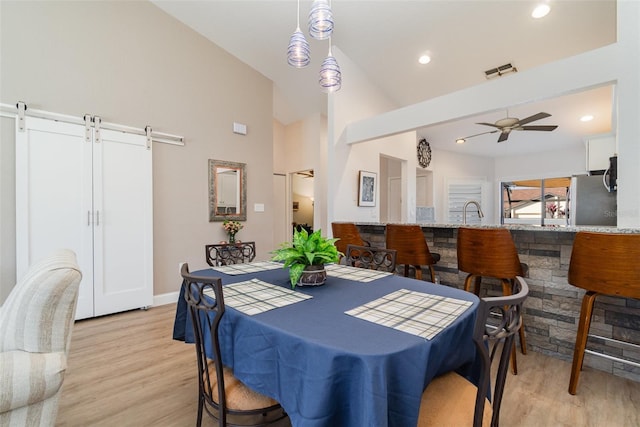 dining area featuring ceiling fan, light hardwood / wood-style floors, vaulted ceiling, and a barn door