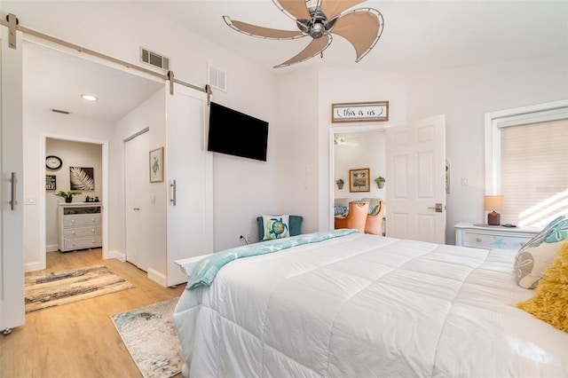 bedroom featuring ceiling fan, a barn door, and light hardwood / wood-style flooring